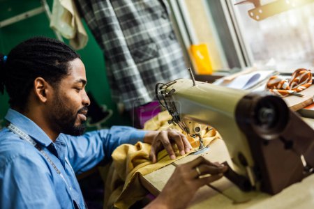 Foto de Hombre afroamericano diseñador de moda de costura en una máquina de coser vintage. - Imagen libre de derechos