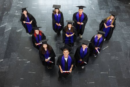 Photo for Group of graduates with togas and diplomas standing happy in the hall and looking at the camera. - Royalty Free Image