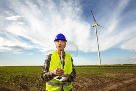 Photo for Engineer looking at wind turbine farm. He is wearing florescent vest and helmet for protection. - Royalty Free Image