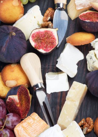 Gourmet-Käseteller mit Brie, Roquefort und Camembert-Käse, Feigen und Käsemessern in Nahaufnahme auf Holzbrett