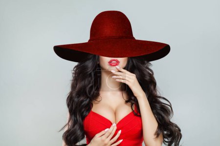 Foto de Belleza femenina perfecta. Retrato de hermosa mujer modelo con pelo largo y maquillaje en rojo sombrero de ala ancha sobre fondo blanco - Imagen libre de derechos