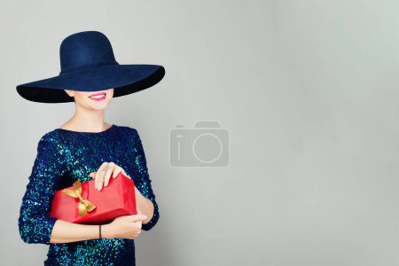 Foto de Mujer feliz en azul amplio sombrero de ala ancha con caja de regalo roja - Imagen libre de derechos