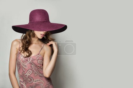Foto de Mujer agradable en vestido sedoso rosa y sombrero de ala ancha rosa sobre fondo blanco, foto de moda - Imagen libre de derechos
