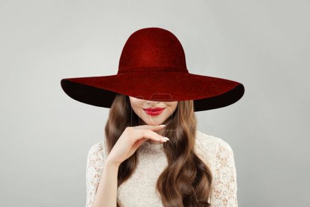 Foto de Hermosa mujer en rojo amplio sombrero de ala ancha. Bonito modelo con maquillaje de labios rojos y lindo retrato de sonrisa sobre fondo blanco - Imagen libre de derechos