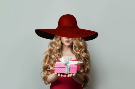 Foto de Mujer encantadora en amplio sombrero de ala ancha rojo con regalo sobre fondo blanco - Imagen libre de derechos