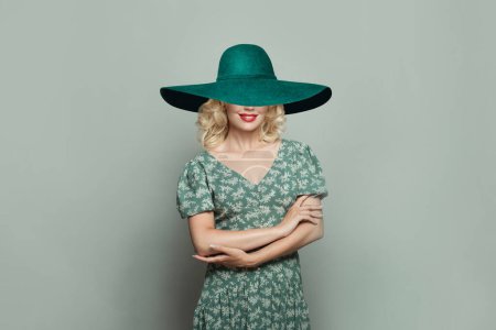 Foto de Hermosa mujer con maquillaje y cabello rubio rizado con sombrero de ala ancha verde sobre fondo verde claro - Imagen libre de derechos