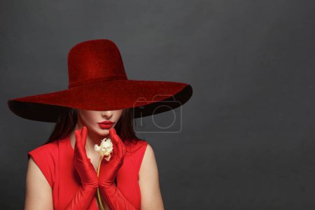 Foto de Día de San Valentín. Mujer cariñosa. Hermosa modelo femenina en un vestido rojo y sombrero de ala ancha rojo sobre negro. - Imagen libre de derechos