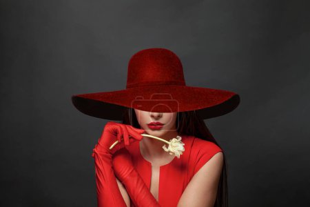 Foto de Retrato de una hermosa joven morena en vestido rojo y sombrero rojo de ala ancha sobre negro - Imagen libre de derechos