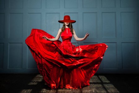 Foto de Hermosa mujer modelo de moda en vestido rojo sedoso y sombrero de ala ancha rojo. Mujer hermosa, retrato completo - Imagen libre de derechos