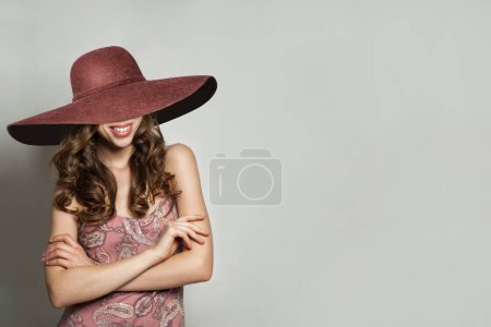 Foto de Glamorosa mujer en vestido de verano y amplio sombrero de ala ancha rosa contra fondo de pared blanca, retrato de moda - Imagen libre de derechos