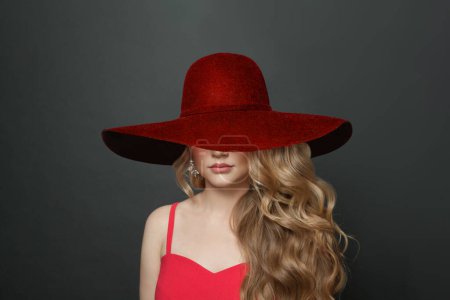 Foto de Mujer rubia celebridad con maquillaje y largo peinado rizado en rojo sombrero de ala ancha sobre fondo negro - Imagen libre de derechos
