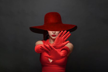 Foto de Basta de gestos. Manos de mujer morena en guantes sedosos rojos y amplio sombrero de ala ancha que muestra gesto de stop, negación, negación y no. Detener el concepto de violencia - Imagen libre de derechos
