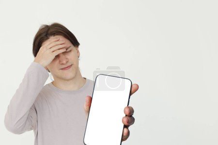 Photo for Confused young adult man showing blank cell phone with empty white screen display, mockup banner - Royalty Free Image