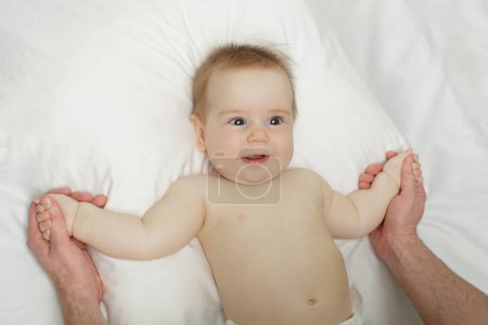 Téléchargez les photos : Petit enfant couché dans un lit blanc, rit et se livre - en image libre de droit