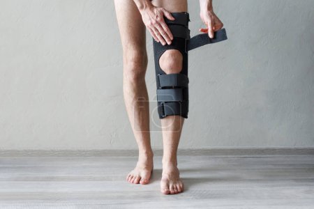 Männliches Bein mit Knieschiene auf grauem Hintergrund. Orthopädische anatomische Orthese. Zahnspangen für Kniefixierung, Verletzungen und Schmerzen. Tutor für Fußorthesen