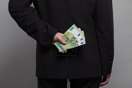 Téléchargez les photos : Un homme d'affaires qui cache de l'argent en euros derrière son dos. Homme d'affaires avec billets en euros en espèces - en image libre de droit