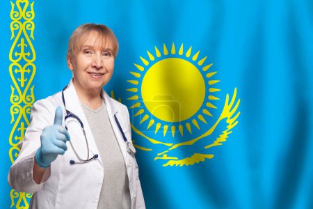 Téléchargez les photos : Kazakh souriant mature médecin femme tenant stéthoscope sur drapeau du Kazakhstan fond - en image libre de droit