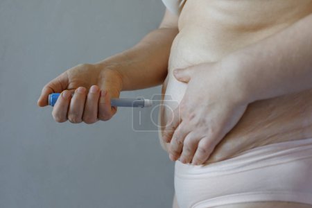 Pluma de inyección azul semaglutida y primer plano del cuerpo femenino sobre fondo gris. Hormona semaglutida utilizada como medicamento para mejorar el azúcar en sangre y la pérdida de peso. 