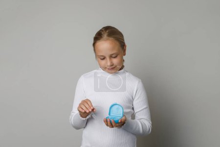 Enfant fille mignonne portant un t-shirt blanc tenant un aligneur invisible, des bretelles ou un ensemble d'hygiène blanchissant sur fond de mur de studio blanc. Concept de soins dentaires