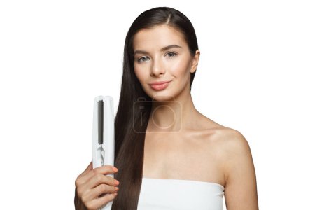 Téléchargez les photos : Femme mannequin tenant le fer à repasser et redressant ses longs cheveux noirs en bonne santé isolés sur fond blanc. Coiffure et coiffure concept - en image libre de droit