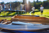 Large cardboard boxes with iron beams and other kit to assemble a netted trampoline as in the background next to people assembling a trampoline on a backyard lawn hoodie #634856288