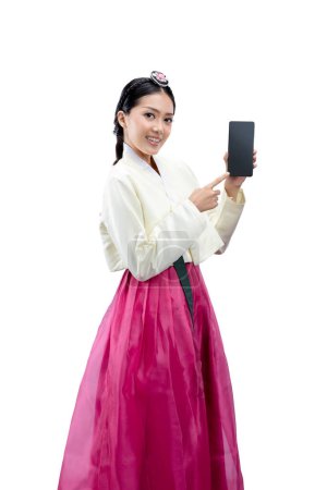 Foto de Mujer asiática vestida con un traje nacional coreano tradicional, Hanbok, de pie mientras muestra la pantalla vacía en el teléfono móvil aislado sobre fondo blanco - Imagen libre de derechos