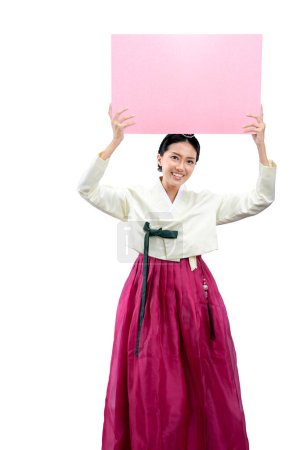 Photo for Asian woman wearing a traditional Korean national costume, Hanbok, standing while holding empty paper for copy space isolated over white background - Royalty Free Image