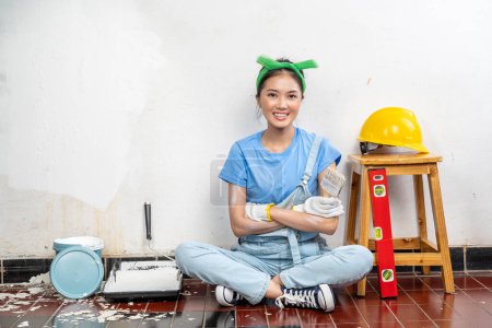 Téléchargez les photos : Asian young housewife in a glove holding a paintbrush with white wall background - en image libre de droit