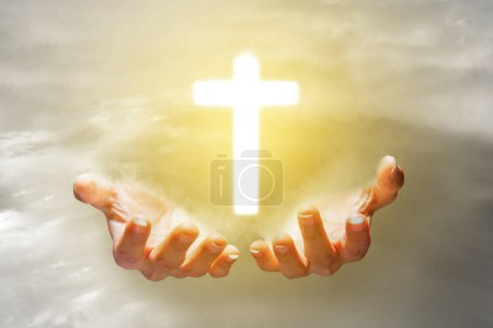 Foto de Mano humana mostrando cruz cristiana con fondo de cielo al atardecer - Imagen libre de derechos