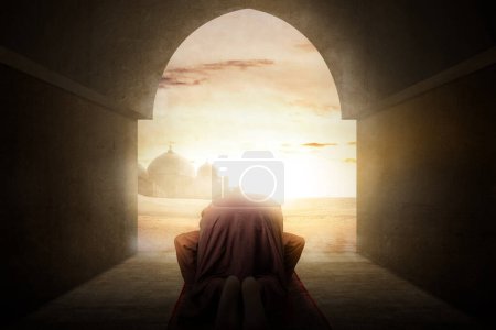 Foto de Hombre musulmán con barba vestida de keffiyeh con agal en posición de oración (salat) en la alfombra de oración dentro de la mezquita - Imagen libre de derechos