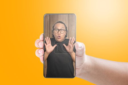 Téléchargez les photos : Portrait d'un homme asiatique avec une expression faciale heureuse sur l'écran du téléphone mobile. Concept de visage de mème - en image libre de droit