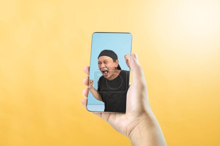 Téléchargez les photos : Portrait d'un homme asiatique avec une expression faciale excitée sur l'écran du téléphone mobile. Concept de visage de mème - en image libre de droit
