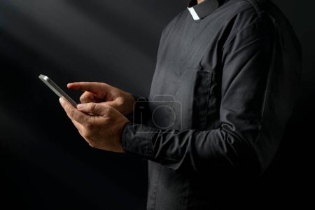 Foto de Retrato de un pastor usando un teléfono móvil sobre un fondo negro. Concepto cristiano - Imagen libre de derechos