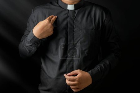 Photo for Young priest doing cross sign on his body isolated on black background. - Royalty Free Image