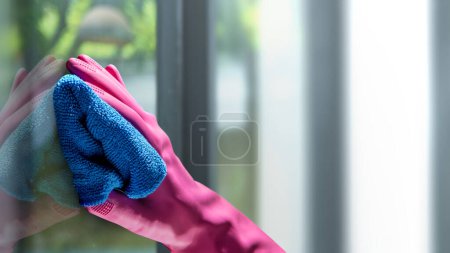 Téléchargez les photos : Main humaine en gant de protection essuyant à l'aide d'un chiffon pour nettoyer la fenêtre. Concept de propreté - en image libre de droit