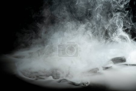 Téléchargez les photos : Fumée blanche tourbillonnante sur un fond sombre. Contexte abstrait - en image libre de droit