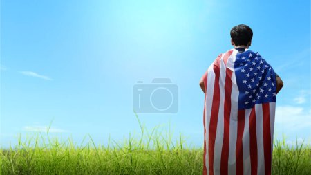 Foto de Portrait of a rear man wearing an American flag on his back with a blue sky background. 4th of July concept - Imagen libre de derechos