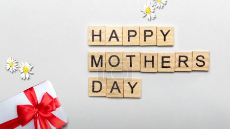 Téléchargez les photos : Une rangée de cubes en bois avec texte de la fête des mères heureux et une boîte-cadeau sur un fond blanc. Concept de fête des mères - en image libre de droit