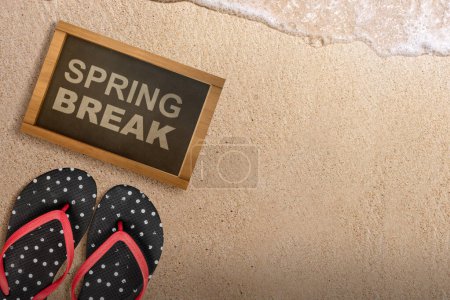 Hausschuh und kleine Kreidetafel mit Spring Break Text am Sandstrand. Frühjahrspause-Konzept