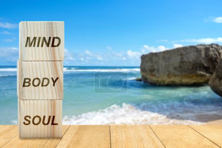 Foto de Stack of small wooden cubes with the text of mind, body, and soul on the table on the beach background. Health mindfulness concept - Imagen libre de derechos