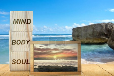 Foto de Stack of small wooden cubes with the text of mind, body, and soul with a small chalkboard with a view of the sunset scene on the beach on the table. Health mindfulness concept - Imagen libre de derechos