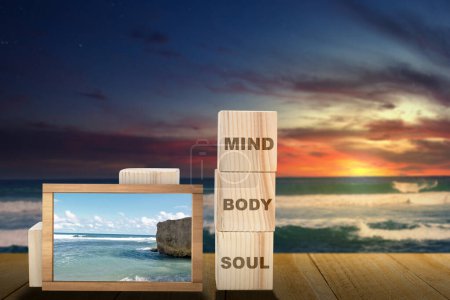 Foto de Stack of small wooden cubes with the text of mind, body, and soul with a small chalkboard with a view of the blue sky on the beach on the table. Health mindfulness concept - Imagen libre de derechos