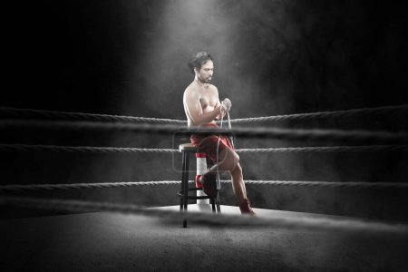 Photo for Portrait of a boxing man sitting and wrapping his hand with tape in the boxing ring - Royalty Free Image