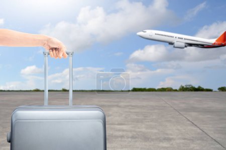 Foto de Una mano humana sosteniendo una maleta con un avión volando sobre un fondo azul del cielo. Listo para viajar. Concepto de viaje - Imagen libre de derechos