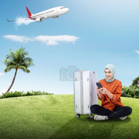 Photo for Portrait of a woman in hijab with a suitcase using a mobile phone while traveling with an airplane flying on a blue sky background. Traveling concept - Royalty Free Image