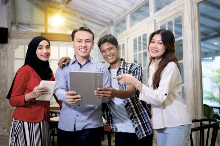 Photo for Multiracial businesspeople smilling for a meeting in cafe or restaurant and pointing digital tablet.  Group of young Indonesian entrepreneurs working together in a modern workplace for new strategy. - Royalty Free Image