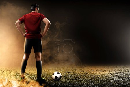 Foto de Retrato de un jugador de fútbol masculino de pie en el campo con la pelota con un fondo de escena dramática - Imagen libre de derechos