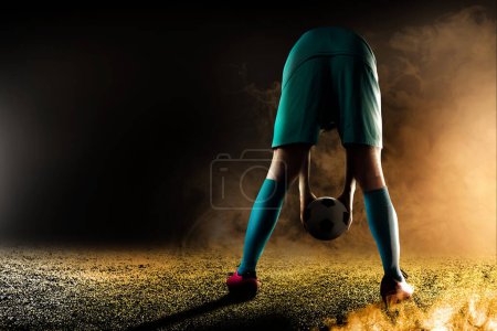 Photo for Portrait of a male football player put the ball on the pitch with a dramatic scene background - Royalty Free Image