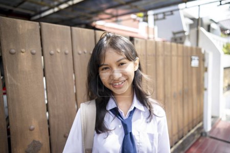 Foto de Joven mujer indonesia con uniforme escolar hich junior ir a la escuela por la mañana en frente de la casa. Regreso al concepto escolar. - Imagen libre de derechos