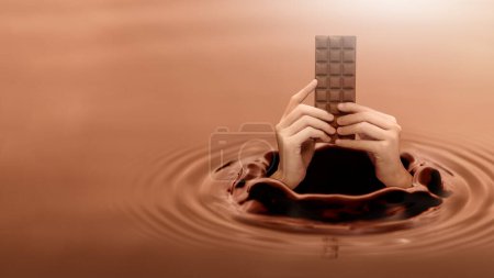 Foto de Close up human hand holding a chocolate bar that appears on the surface of a chocolate liquid, concept of giving on world chocolate day. Sweet and energy snack. Mock up deisign. - Imagen libre de derechos